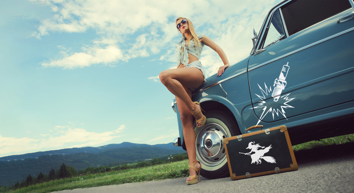 Junge Frau lehnt an Oldtimer mit Autotattoo und Koffer mit Aufkleber