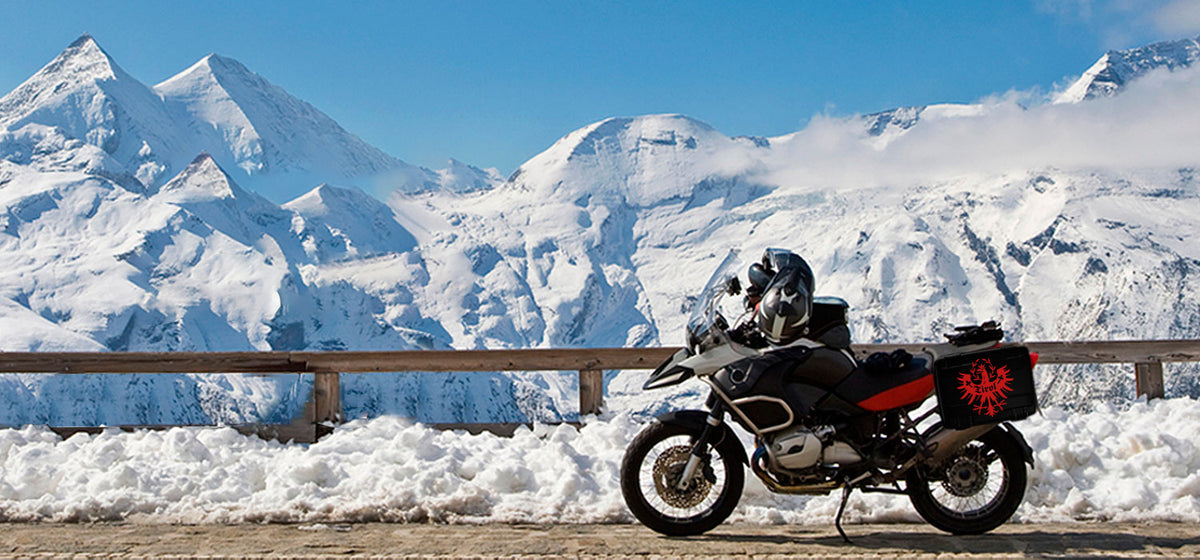 Motorrad vor verschneiter Bergkulisse mit Tiroler Adler auf dem Motorradkoffer